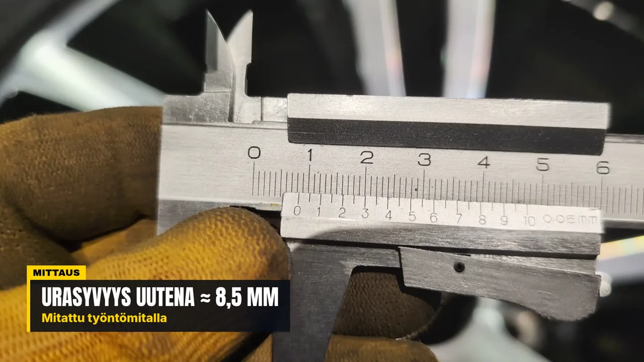 A gloved hand holding a vernier caliper on the tread of a new studded tyre, with the reading about 8.5 mm