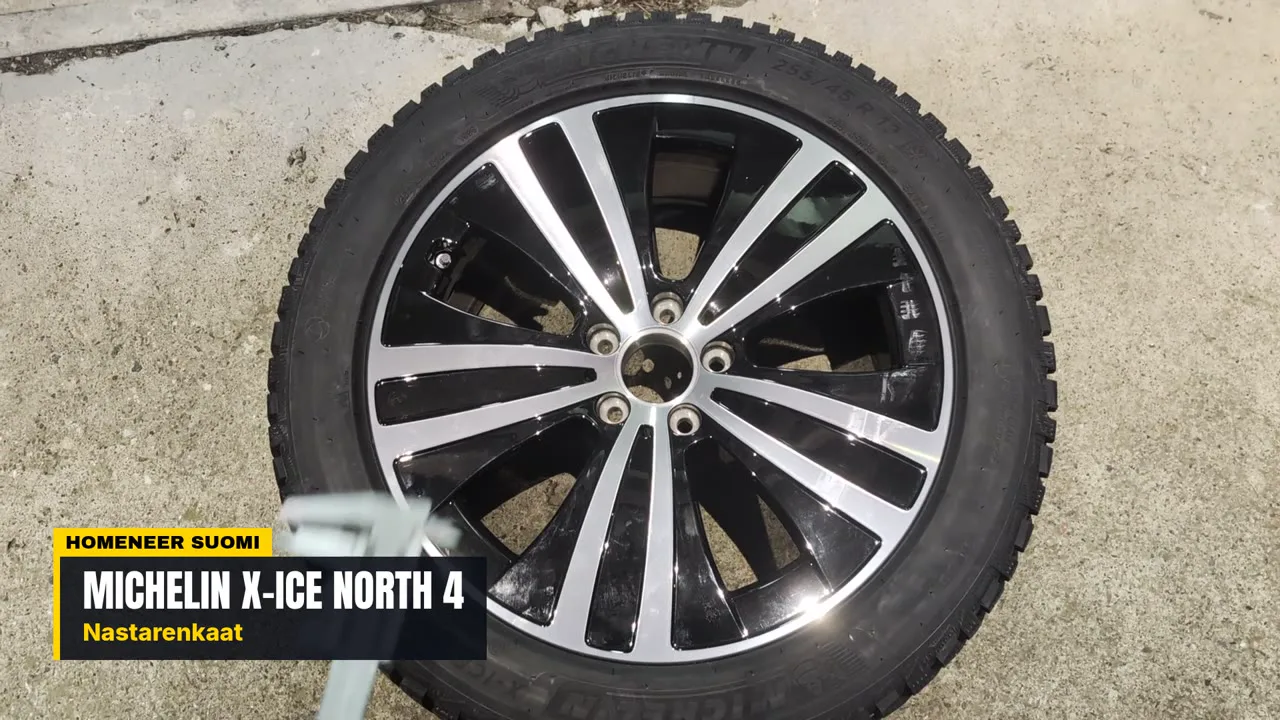 Michelin X-Ice North 4 studded tyre mounted on a black and silver alloy wheel, lying on a concrete floor
